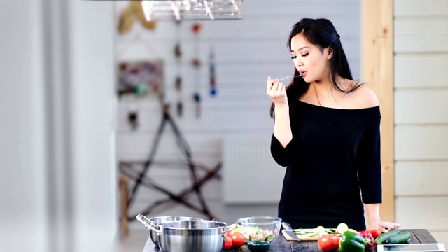 可爱的年轻亚洲女人烹饪和吃新鲜健康的食物在厨房中中长期视频素材