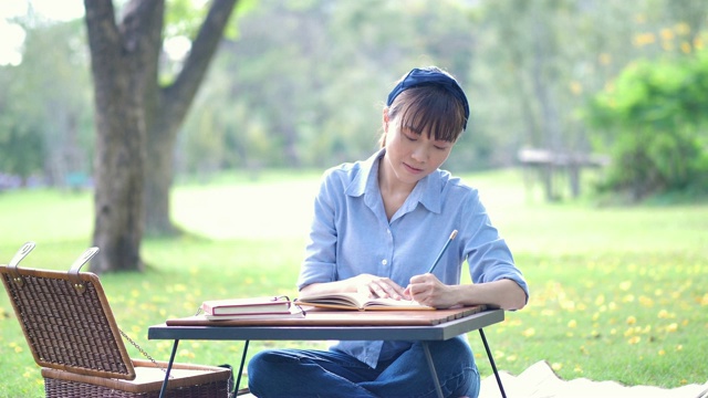 年轻美丽的亚洲女人写在笔记本上在自然或公园和阳光。清新快乐放松视频素材