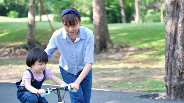 亚洲家庭与母亲教她的女儿或孩子女孩骑自行车在自然或公园和阳光下玩。慢动作视频素材