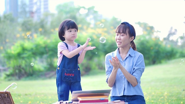 亚洲家庭与母亲和女儿或孩子女孩吹肥皂泡，唱歌，跳舞，跳跃，在自然公园和阳光下玩耍。慢动作视频素材