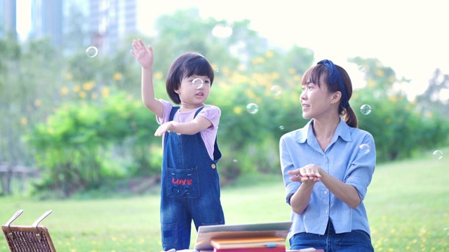 亚洲家庭与母亲和女儿或孩子女孩吹肥皂泡，唱歌，跳舞，跳跃，在自然公园和阳光下玩耍。慢动作视频素材