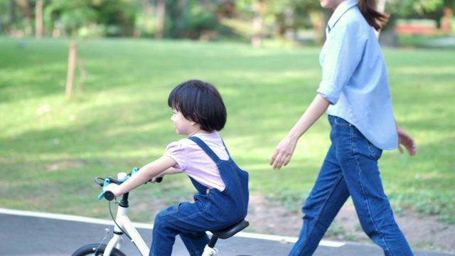 亚洲家庭与母亲教她的女儿或孩子女孩骑自行车在自然或公园和阳光下玩。慢动作视频素材