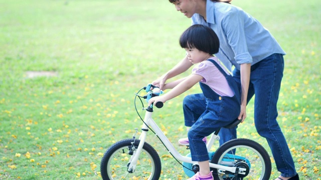 亚洲家庭与母亲教她的女儿或孩子女孩骑自行车在自然或公园和阳光下玩。慢动作视频素材