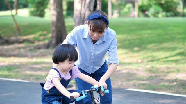 亚洲家庭与母亲教她的女儿或孩子女孩骑自行车在自然或公园和阳光下玩。慢动作视频素材