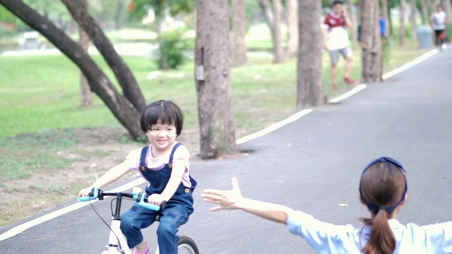 亚洲家庭与母亲和女儿或孩子女孩骑自行车在公路上的自然或公园和阳光。慢动作视频素材