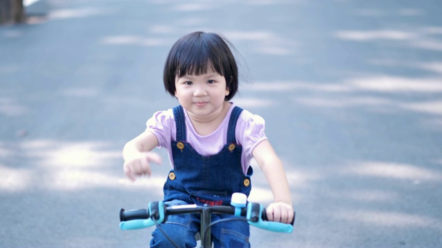 亚洲儿童女孩骑自行车在自然或公园和阳光的道路上有乐趣。慢动作视频素材