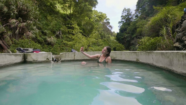 年轻女子正在热浴自拍手机。女性美容博主在泡温泉时用智能手机自拍。天然水疗和身体治疗。视频素材