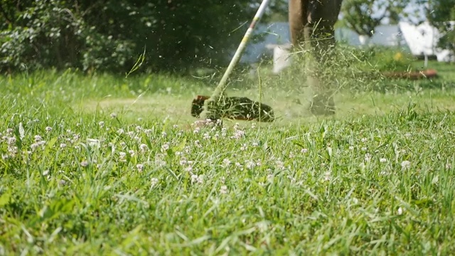 男工人在一个阳光明媚的夏日用汽油割草机修剪草坪。在乡下割草。Slowmotion视频素材