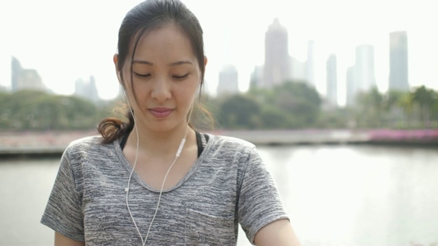 一个漂亮的健康女人的肖像戴着耳机在户外检查她的智能手表在城市视频素材