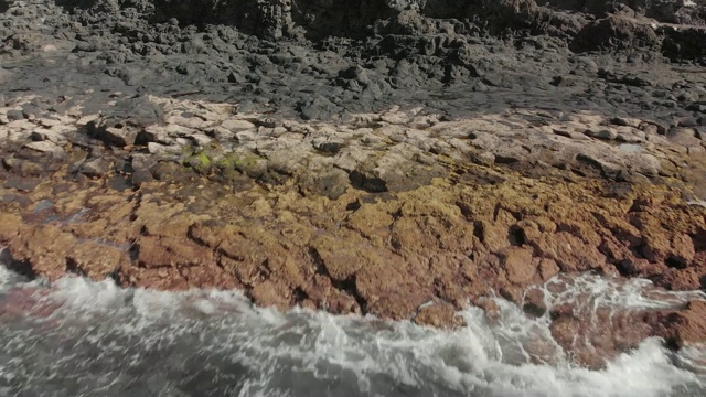 空中射击。海洋海岸线的火山表面。深灰色和黄色石头的特写。多莉拍摄的是碧绿的海浪视频素材