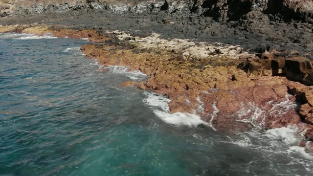 空中射击。沿着火山海岸飞行。这里的景色是黄色和棕色的大石头，周围是绿松石般的海浪拍打着海滩。特写镜头视频素材