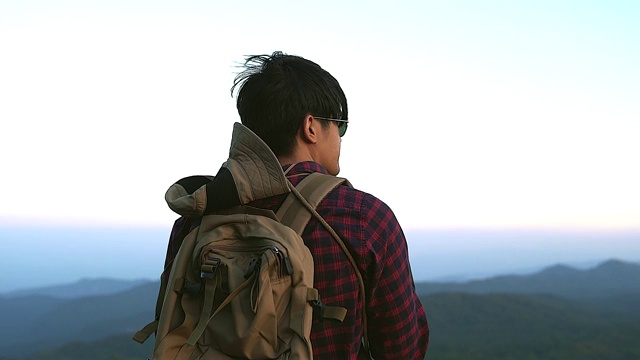 一名年轻的游客正在山顶徒步旅行，观赏美丽的风景。视频素材