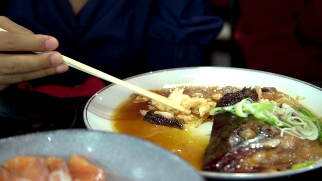 特写:年轻的亚洲女人吃煮鲑鱼头和甜酱(鲑鱼Kabutoni)寿司卷和日本食物。视频素材