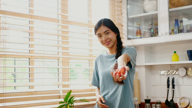 年轻的亚洲女人在家里的厨房里吃着幸福的草莓，人们健康的生活方式视频素材