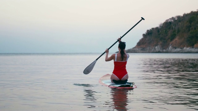 女人在红色泳衣上SUP站立桨板在海湾日落视频素材