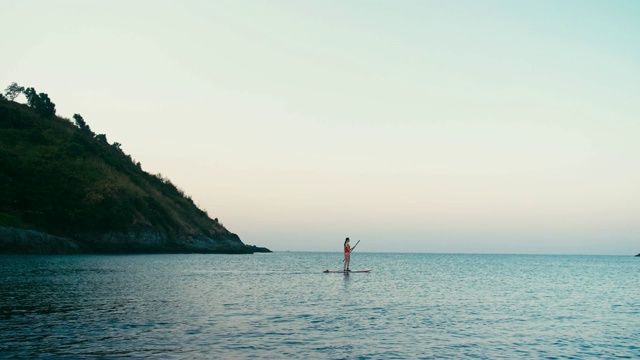 女人在红色泳衣上SUP站立桨板在海湾日落视频素材