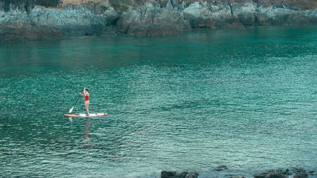 女人在红色泳衣上SUP站立桨板在海湾日落视频素材