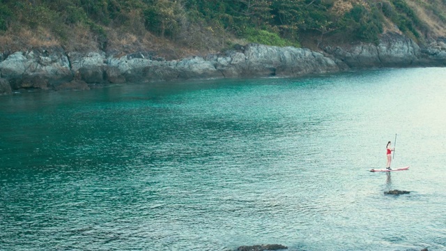 女人在红色泳衣上SUP站立桨板在海湾日落视频素材