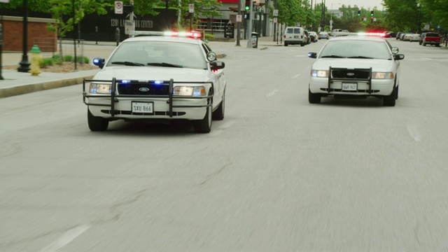 一辆车在街上疾驰，后面跟着两辆警灯闪烁的警车。(车牌不是真的，车牌是道具。)视频素材