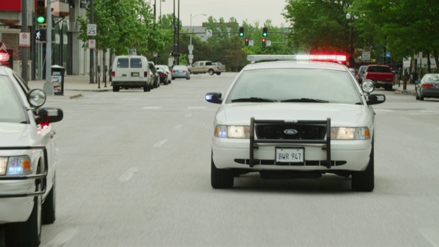 一辆车在街上疾驰，后面跟着两辆警灯闪烁的警车。(车牌不是真的，车牌是道具。)视频素材