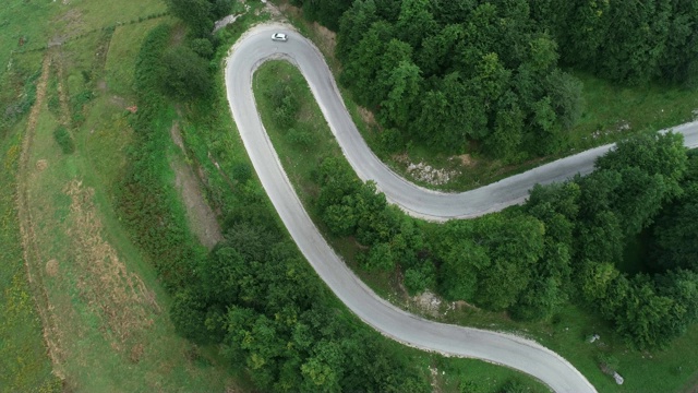 航拍下了一条穿过群山的道路和一辆汽车在路上行驶的画面视频素材