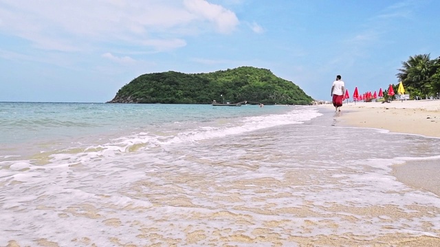 一个年轻英俊的男人正在热带岛屿的海滩上散步。视频素材