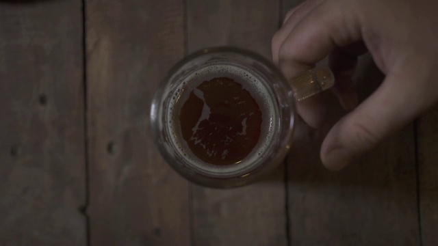 啤酒杯站在酒吧酒吧的木桌上俯视图。男子手拿啤酒杯在酒吧喝酒视频素材