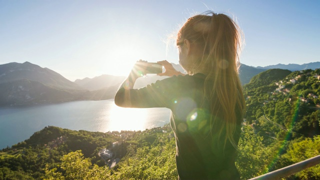 一名女游客以欧洲阿尔卑斯山为背景，拍摄意大利科莫湖和湖滨村庄的全景视频素材