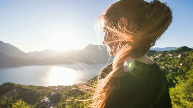 在一个阳光明媚的夏日，俯瞰着山湖和湖滨村庄的女人视频素材