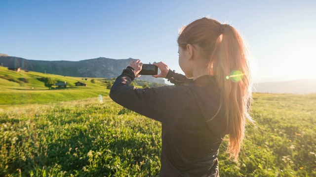 一个女人在春天度假，用智能手机拍摄山景视频素材