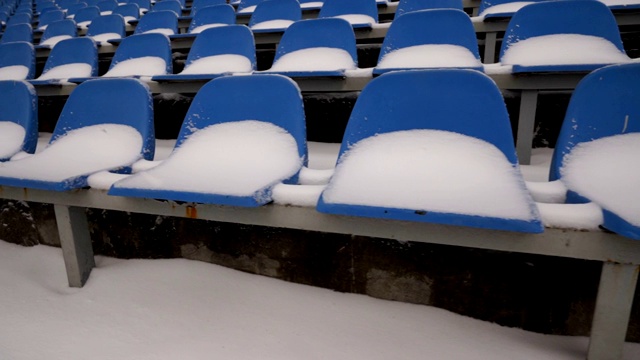 在冬季，体育场看台上一排排被雪覆盖的蓝色塑料座位视频素材