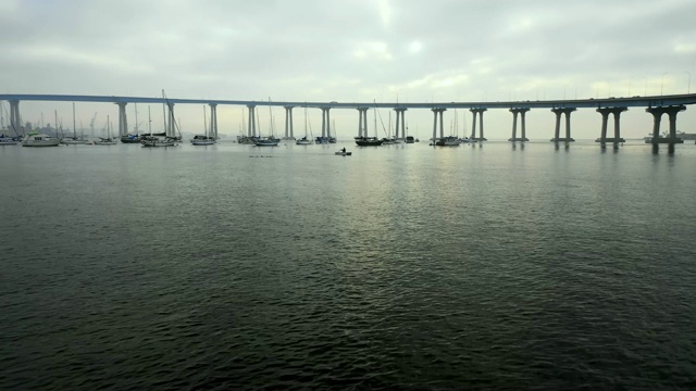 空中向前:美国圣地亚哥阴天桥下海水中漂浮的船只视频素材