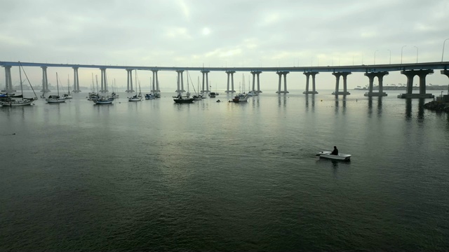 空中封锁:美国圣地亚哥阴天桥下海水中漂浮的船只视频素材