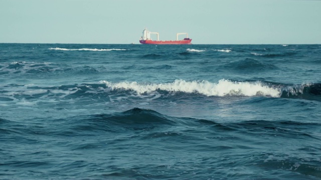 湛蓝的海面上明亮的黎明。海岸。水面上的小波浪。大型商业货船出现在地平线上。Copyspace视频素材