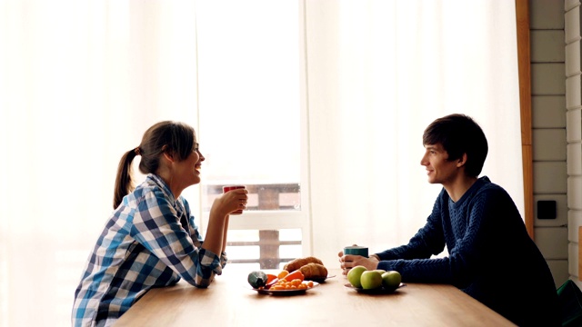 从侧面看，男男女女围坐在厨房里喝茶聊天，在家里享受宁静的早晨。饮料与人的概念。视频素材