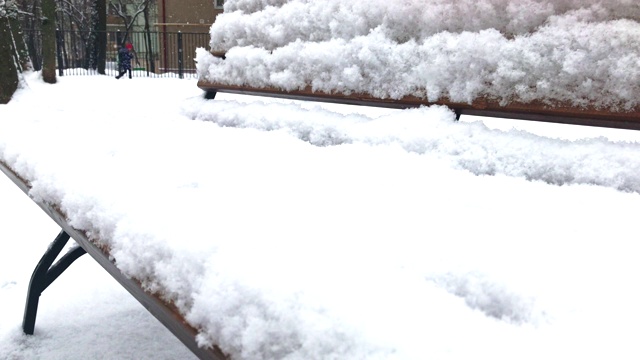 近距离观看一个公园里冬天下雪的长椅，下雪了，背景是一些认不出来的人走过视频素材