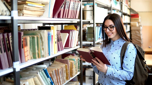 年轻的学生拿着书和背包站在大学图书馆的书架旁视频素材