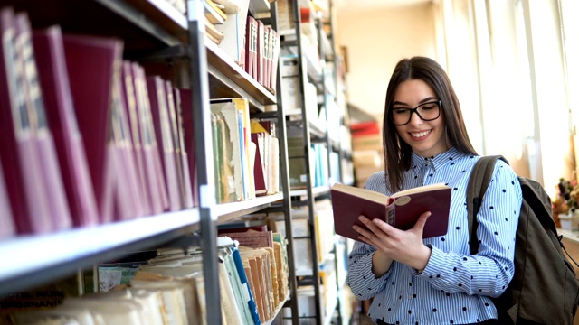 年轻的学生拿着书和背包站在大学图书馆的书架旁视频素材