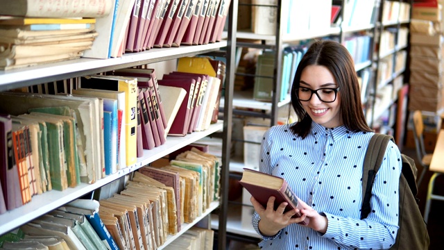 年轻的学生拿着书和背包站在大学图书馆的书架旁视频素材