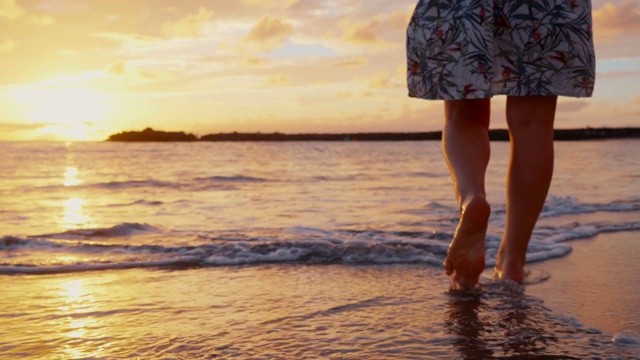 女人赤着脚走在沙滩上，走向海浪和美丽的夕阳视频素材