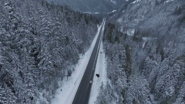 无人机飞行在冬季积雪覆盖的树木附近的道路视频素材