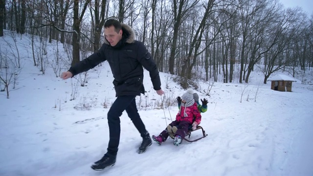 冬天的森林里，父亲拉着孩子们的雪橇在雪道上滑行视频素材