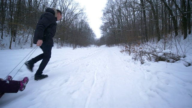 在冬天的森林里度假，爸爸拉着雪橇和孩子们在雪地上奔跑视频素材