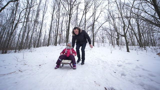 父亲在寒假里用雪橇把小女儿从雪山上拉下来视频素材