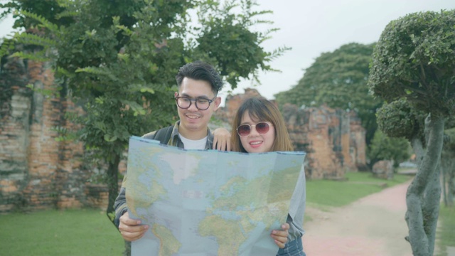 旅行者亚洲夫妇在泰国大城府度假时，一边看地图一边指路，背包客夫妇享受在传统城市的旅程。情侣旅行的生活方式概念。视频素材