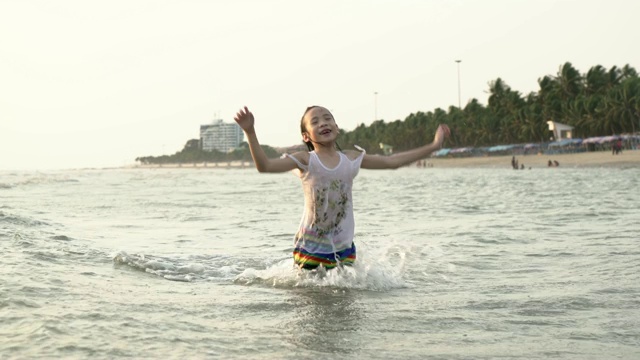 小亚洲女孩快乐地跑和跳在海滩上的海浪。小女孩在海边玩耍。视频素材