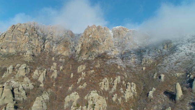 在阳光明媚的日子里，被巨大的岩石和灌木覆盖的雪山峭壁映衬着美丽的蓝天。美妙的山景视频素材