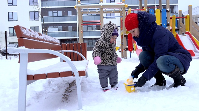 冬天，妈妈和女儿在五彩缤纷的操场上玩雪。4 k视频素材