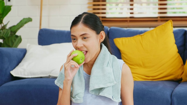 年轻的亚洲女子吃青苹果后在家客厅锻炼，人与健康的生活方式，幸福视频素材