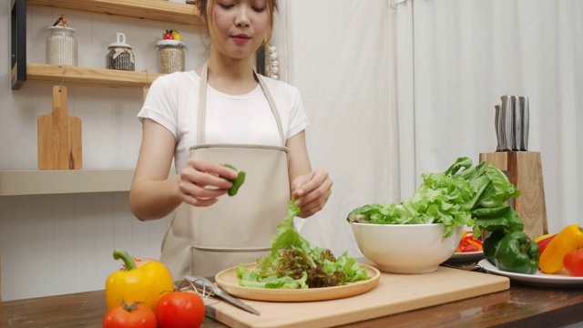 博主亚洲妇女在家里厨房做沙拉健康食物。女性准备食物的概念。视频购买